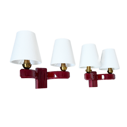 Two matching wall-mounted light fixtures with white tapered lampshades and glossy deep red bases, shown on a plain white background.