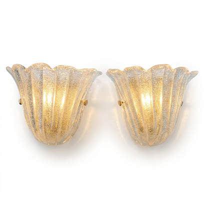A pair of vintage-style wall sconces with fluted, tulip-shaped glass shades. The glass has a textured, crackled finish and glows with a warm golden light, mounted on a plain white background.