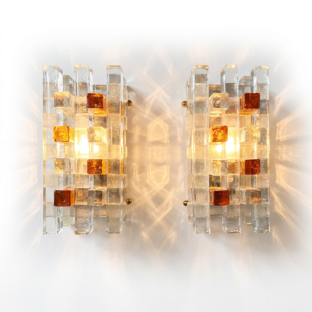 A pair of mid-century modern wall sconces made of clear acrylic blocks with amber-colored glass inserts, glowing with warm light against a white background.