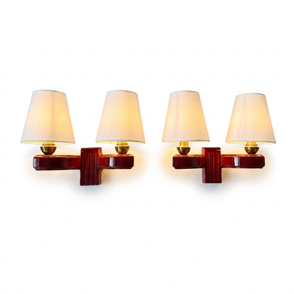 A pair of wall-mounted two-light sconces with tapered off-white fabric shades and glossy dark reddish-brown bases, shown against a plain white background.