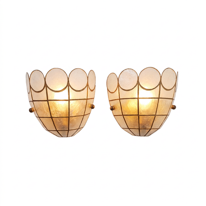A pair of vintage-style wall sconces with scalloped glass shades and a grid pattern, glowing with warm light against a white background.