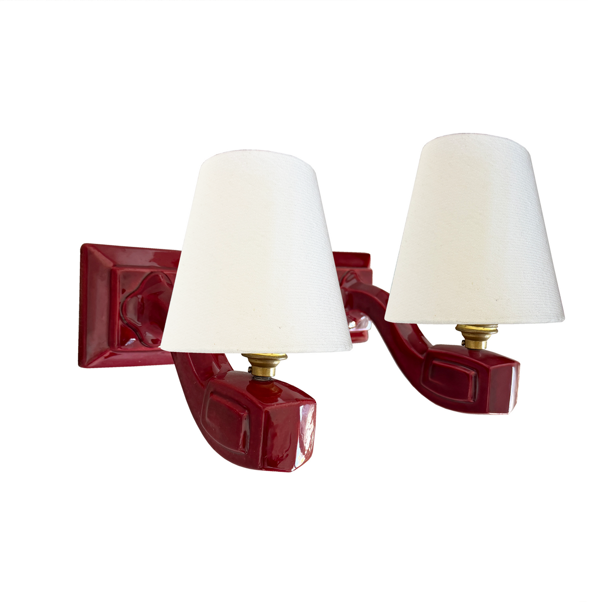 A two-light wall sconce with glossy deep red ceramic arms and white fabric drum shades, shown against a plain white background.