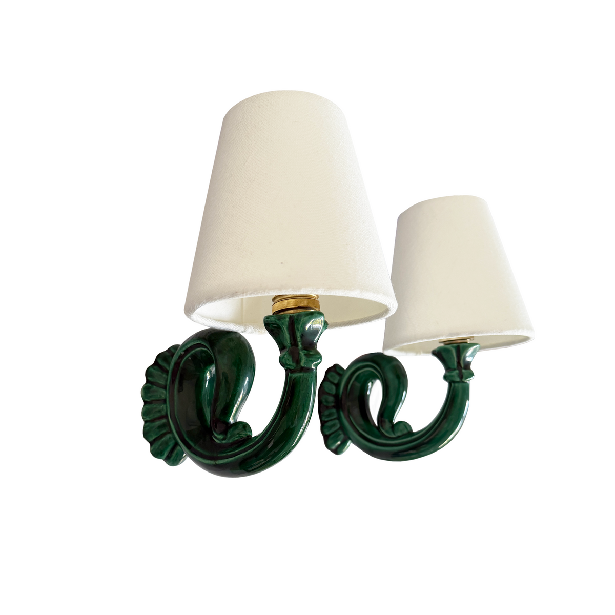 A two-light wall sconce with a glossy dark green ceramic scrollwork base and two tapered off-white fabric shades, shown against a plain white background.