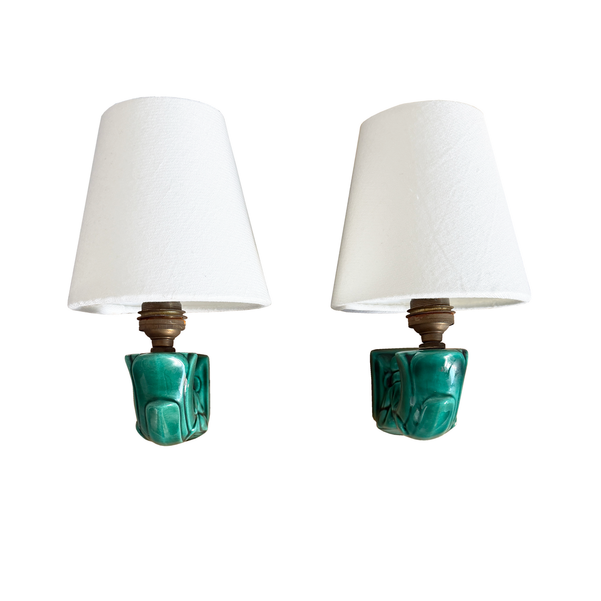 A pair of vintage wall sconces with white tapered fabric shades and carved turquoise green ceramic bases, shown against a plain white background.